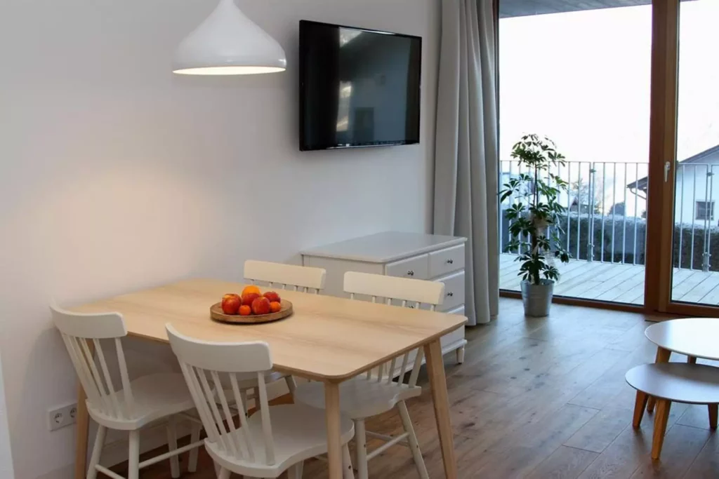 Essbereich mit hellem Holztisch und weißen Stühlen, Obstschale, Wand-TV, Sideboard, Pflanze vor bodentiefem, Referenzen