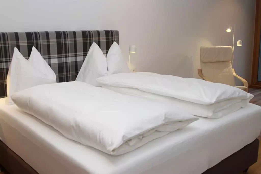 Modernes Schlafzimmer mit Doppelbett, kariertem Polsterkopfteil, weißen Bettdecken und Sessel in schlichtem, Referenzen