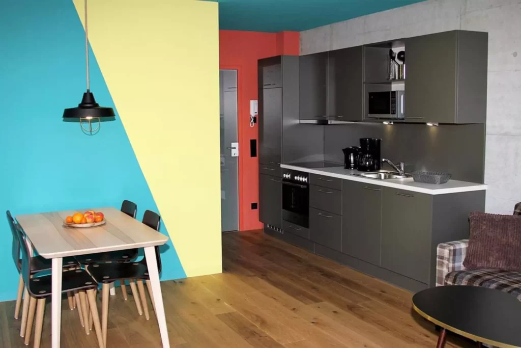 Moderne Küchenzeile mit grauen Fronten, Essbereich mit Holztisch und schwarzen Stühlen vor farbiger, Referenzen