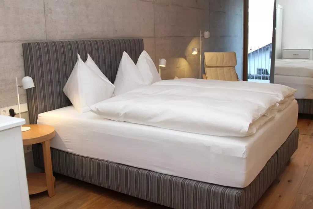 Modernes Schlafzimmer mit gestreiftem Polsterbett, weißer Bettwäsche, Holz-Nachttisch, Leselampen und beiger, Referenzen