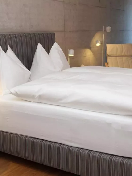 Modernes Schlafzimmer mit gestreiftem Polsterbett, weißer Bettwäsche, Holz-Nachttisch, Leselampen und beiger, Referenzen