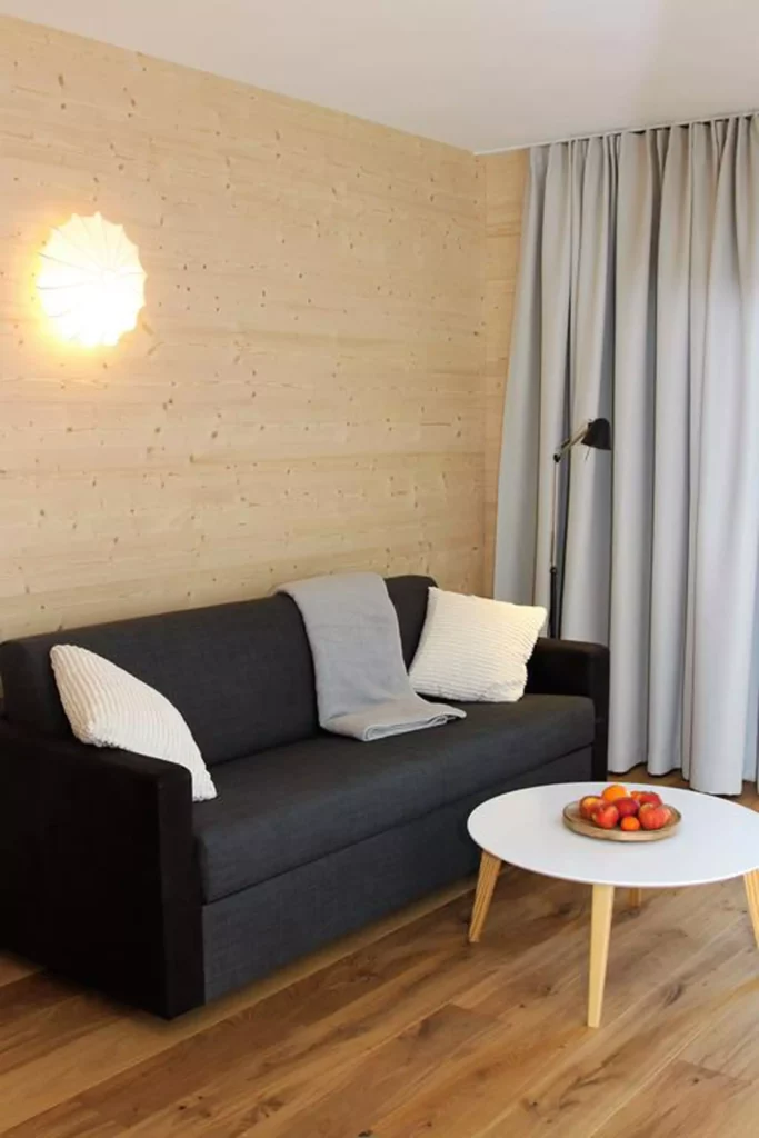 Wohnzimmer mit schwarzem Sofa, weißem Beistelltisch, Holzverkleidung, grauem Vorhang und moderner Wandlampe, Referenzen