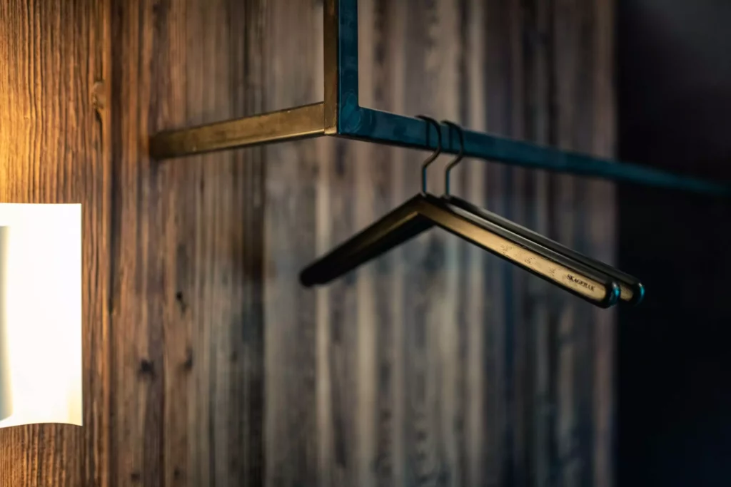 Schwarze Kleiderbügel aus Holz hängen an einem schwarzen Metallkleiderstangenrahmen vor einer dunklen, Minotti