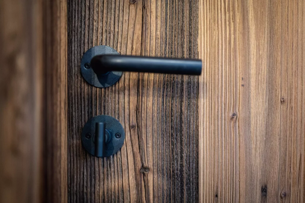 Schwarzer Türgriff und Drehverschluss aus Metall an einer Tür aus massivem Holz mit sichtbarer Maserung, Minotti