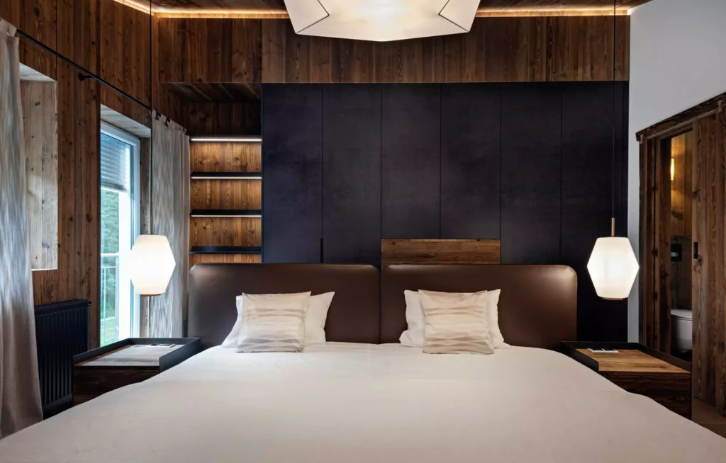 Modernes Schlafzimmer mit braunem Lederbett, weißen Kissen, Holzverkleidung, dunklem Wandpaneel und hängenden, Minotti