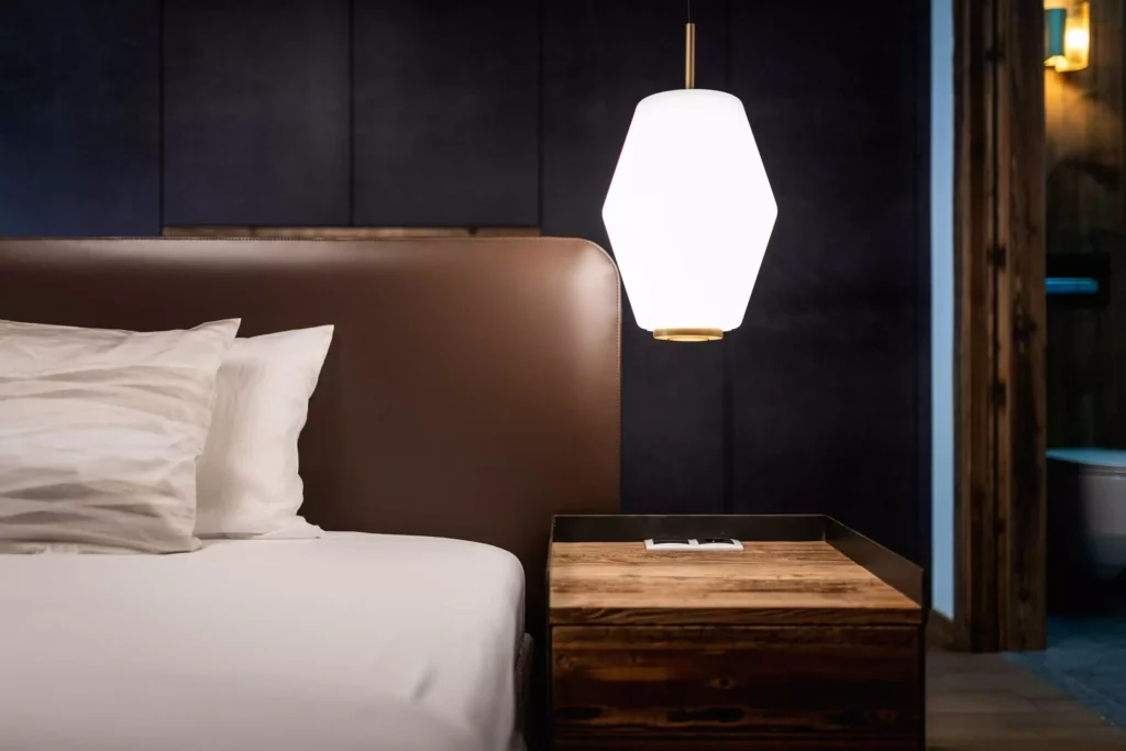 Schlafzimmer mit braunem Leder-Kopfteil, weißer Bettwäsche, hölzernem Nachttisch und moderner Hängeleuchte im Minotti-Design