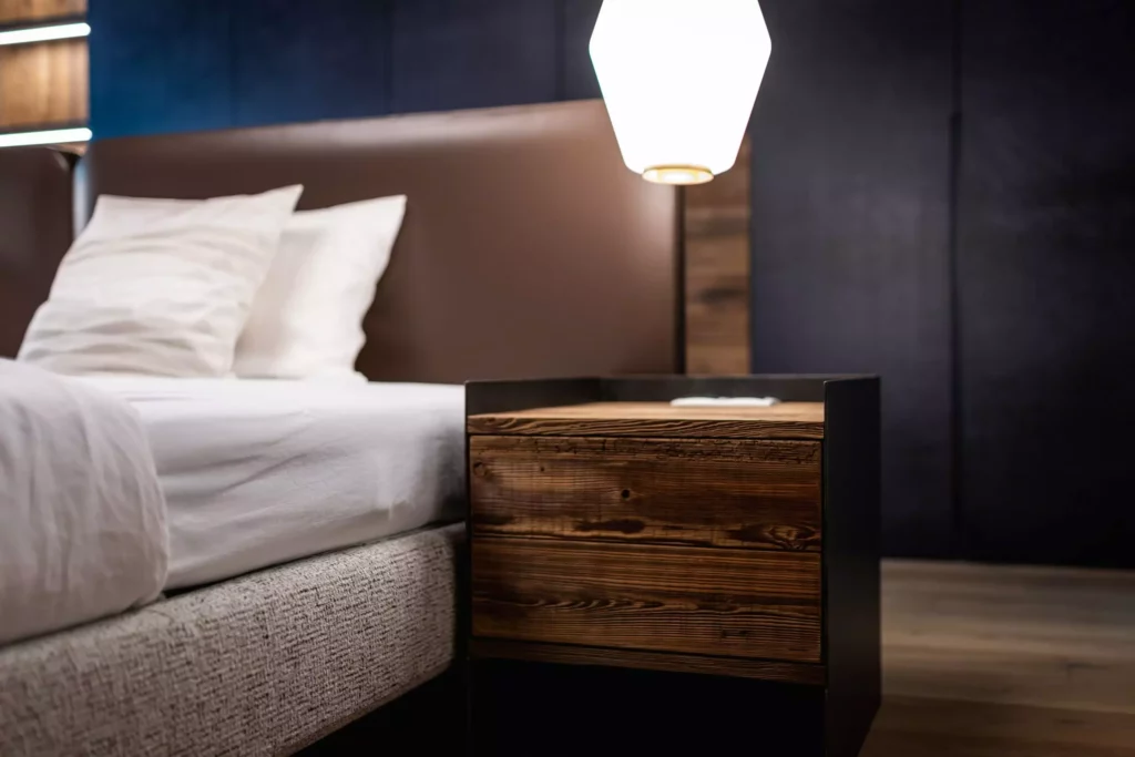 Modernes Schlafzimmer mit braunem Polsterbett, weißer Bettwäsche und Nachttisch aus Massivholz und Metall im Minotti Design