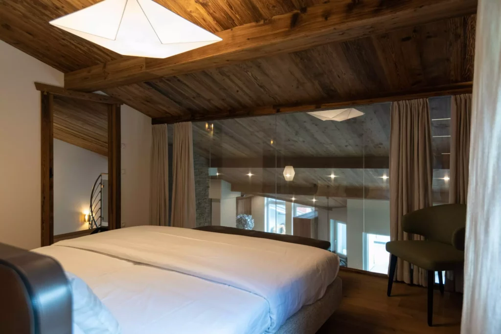 Schlafzimmer mit Massivholzdecke, großem Bett, grünem Stuhl und Glaswand mit Blick in den Wohnraum, Innenarchitektur, Minotti