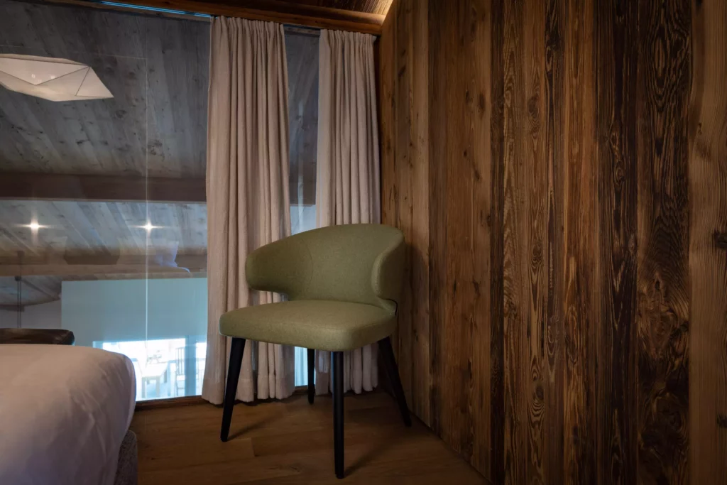 Grüner Polsterstuhl mit schwarzen Beinen in einer Ecke mit Holzverkleidung und Vorhängen im modernen Innenraum eines, Minotti