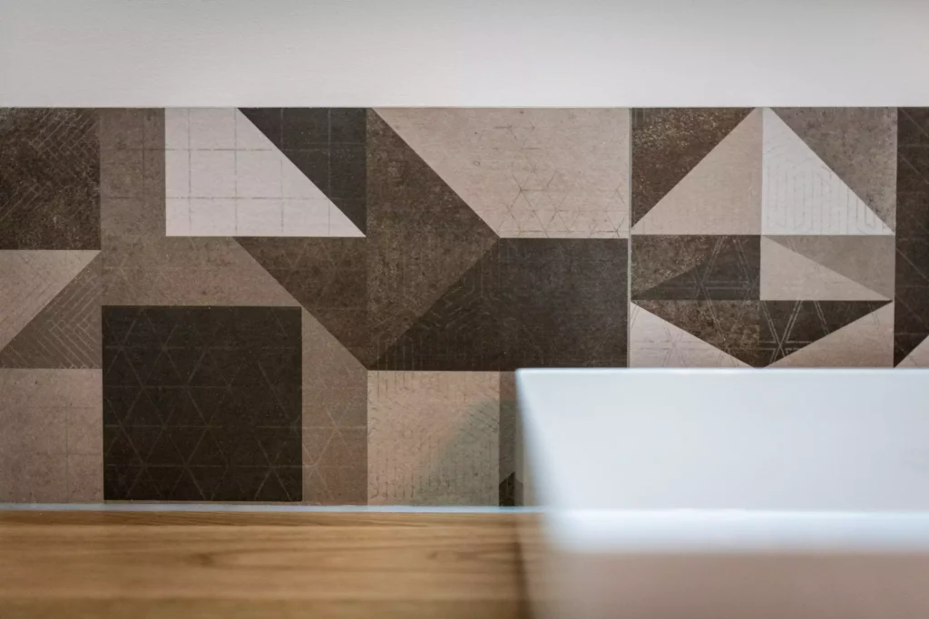 Nahaufnahme einer geometrisch gemusterten Wandfliese in Braun- und Beigetönen mit einem weißen Möbelstück im, Minotti