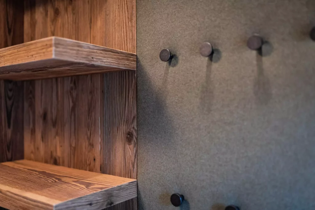Massivholzregal mit sichtbarer Maserung neben grauer Wand mit schwarzen Haken als Teil einer, Minotti