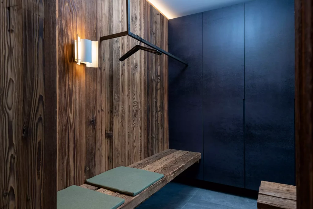 Dunkle Holzbank mit grünen Sitzkissen, Wandlampe und schwarzer Garderobe in modernem Eingangsbereich mit, Minotti