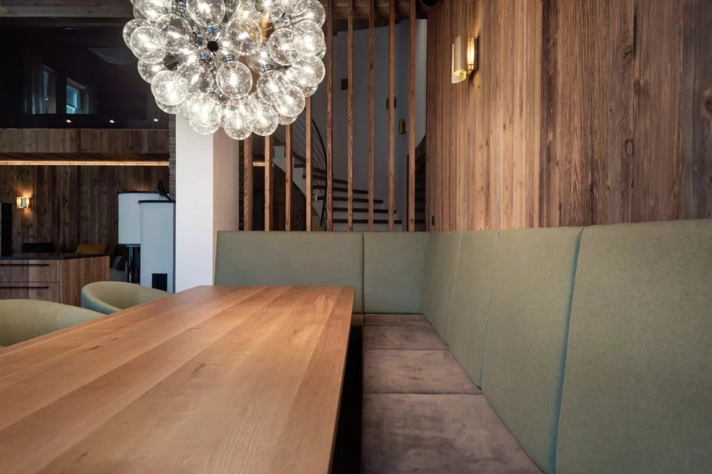 Essbereich mit massivem Holztisch, grüner Polsterbank und moderner Glaskugel-Hängeleuchte in Chalet-Interieur mit, Minotti