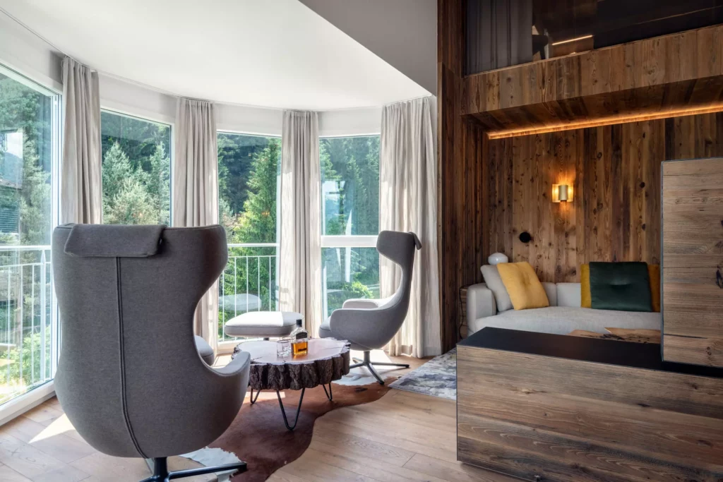 Wohnraum mit großen Panoramafenstern, zwei grauen Design-Sesseln, Baumstamm-Couchtisch und, Minotti