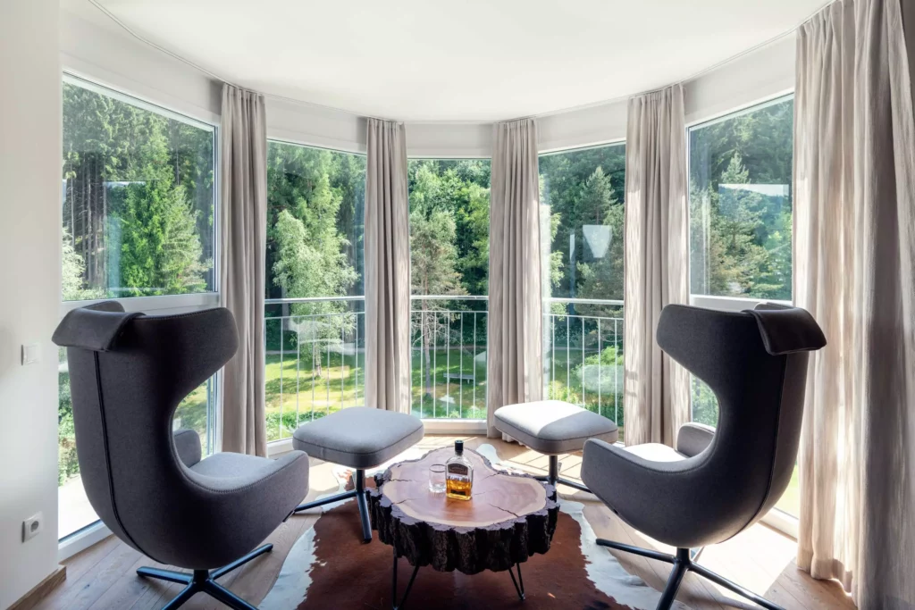 Gemütliche Sitzecke mit zwei grauen Designermöbeln und Hockern vor großen Fenstern mit Blick auf grüne, Minotti