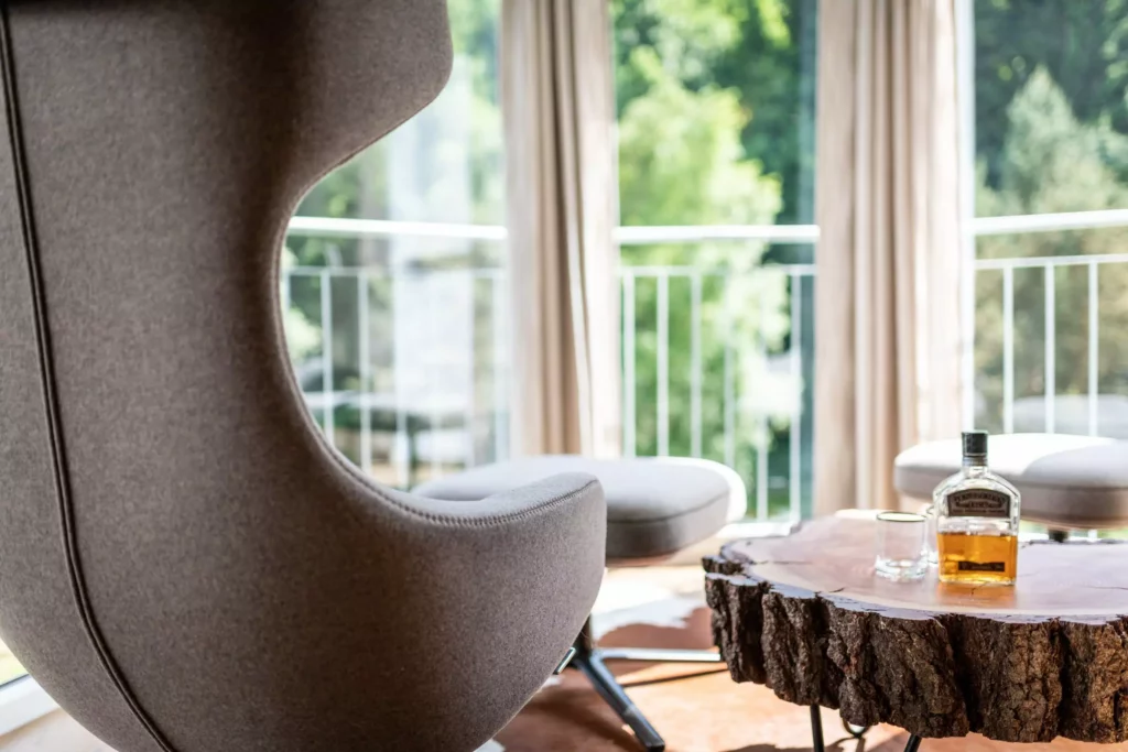 Moderner Lounge-Sessel neben einem Massivholz-Tisch mit Whiskeyflasche und Glas in einem hellen Wohnraum mit Balkon, Minotti