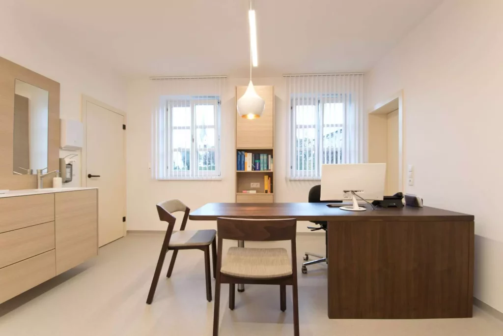 Moderner Besprechungsraum einer Arztpraxis mit maßgefertigtem Holztisch, Stühlen und heller Innenarchitektur in, Referenz