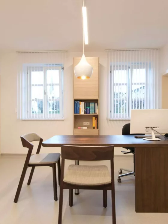 Moderner Besprechungsraum einer Arztpraxis mit maßgefertigtem Holztisch, Stühlen und heller Innenarchitektur in, Referenz