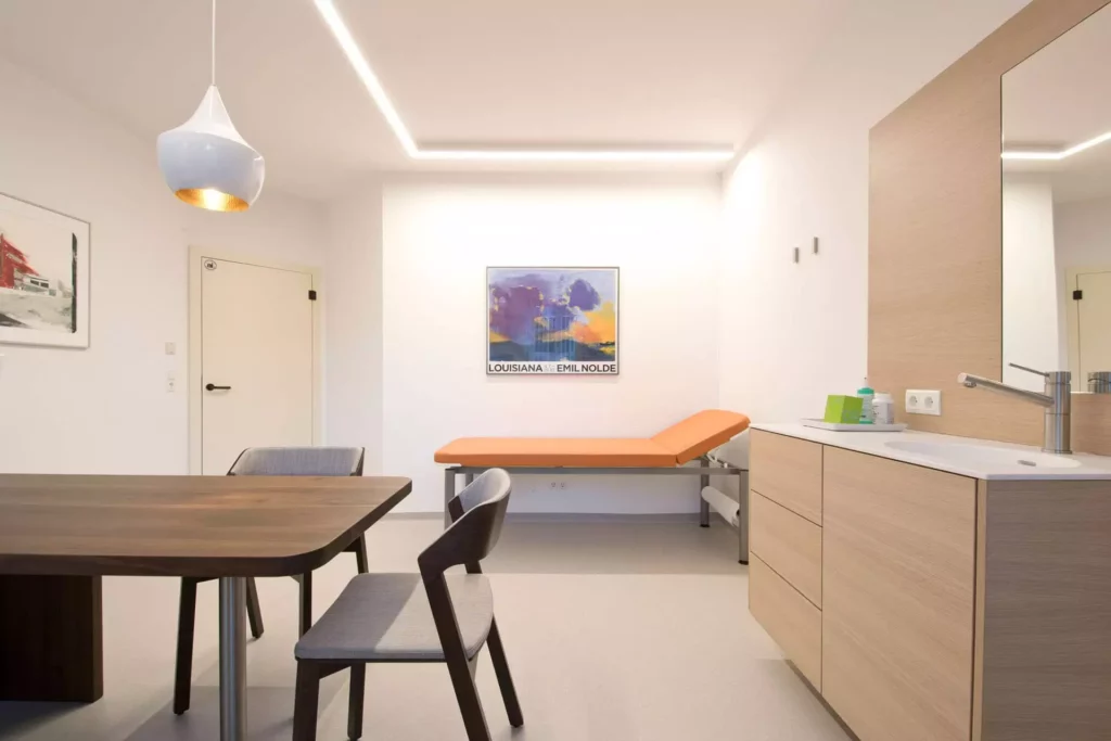 Moderne Arztpraxis Wagrain mit maßgefertigter Tischlerei, orangefarbener Liege, Holz-Möbeln und heller, Referenz