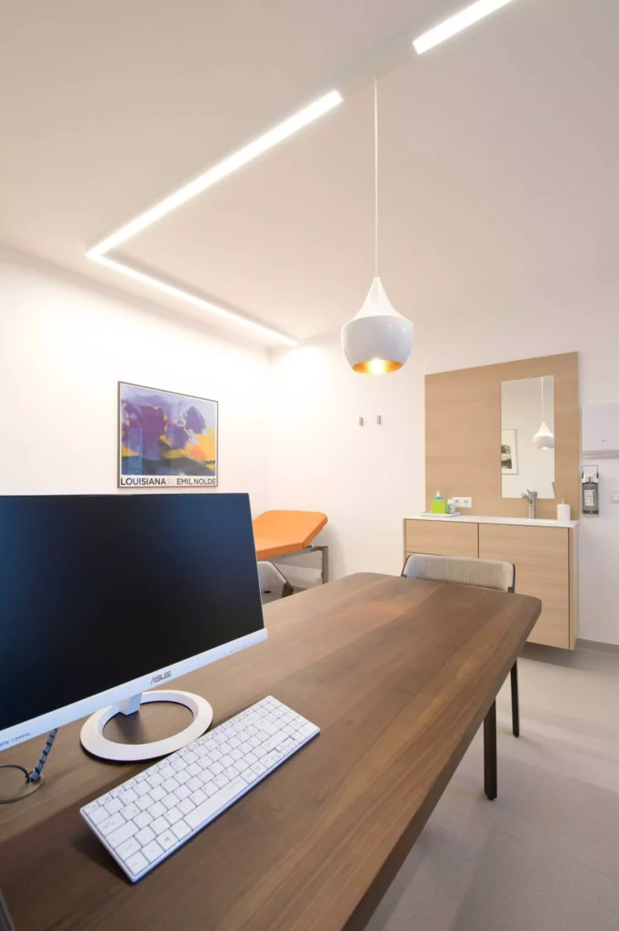 Modern eingerichteter Behandlungsraum einer Arztpraxis in Wagrain mit maßgefertigtem Holztisch, Computer, Referenz