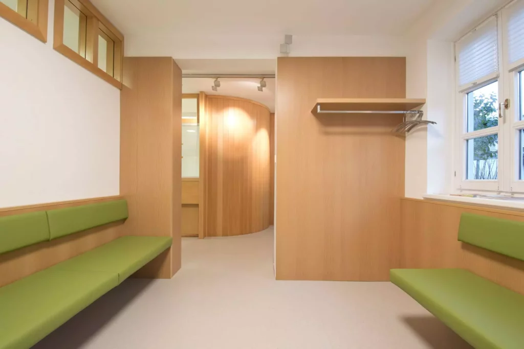 Wartebereich einer Arztpraxis mit maßgefertigten Holzelementen und grünen Sitzbänken in moderner Innenarchitektur, Referenz