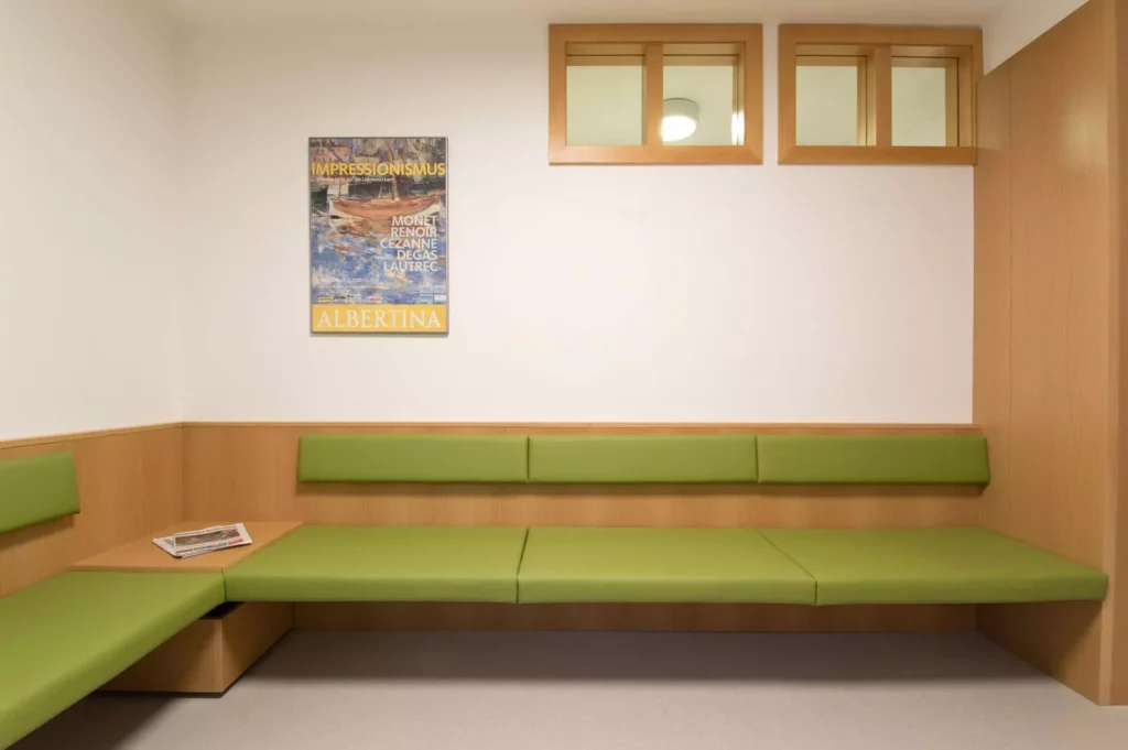 Wartebereich einer Arztpraxis mit maßgefertigter grüner Sitzbank und Holzverkleidung, Impressionismus-Plakat an, Referenz