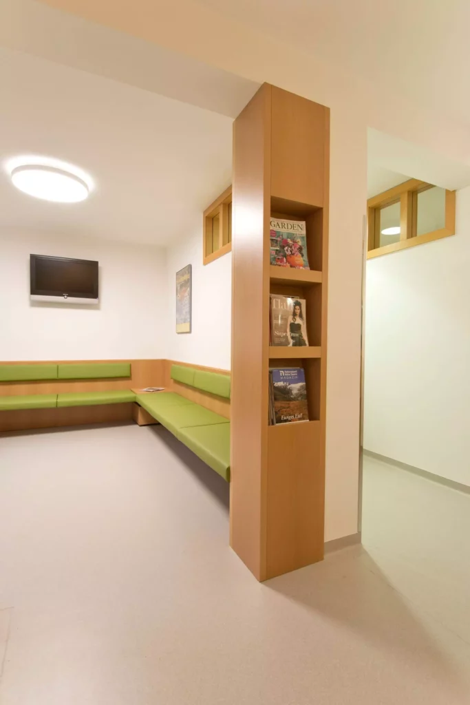 Wartezimmer einer Arztpraxis mit maßgefertigter Holzbank mit grünen Polstern und integriertem Zeitschriftenregal, Referenz