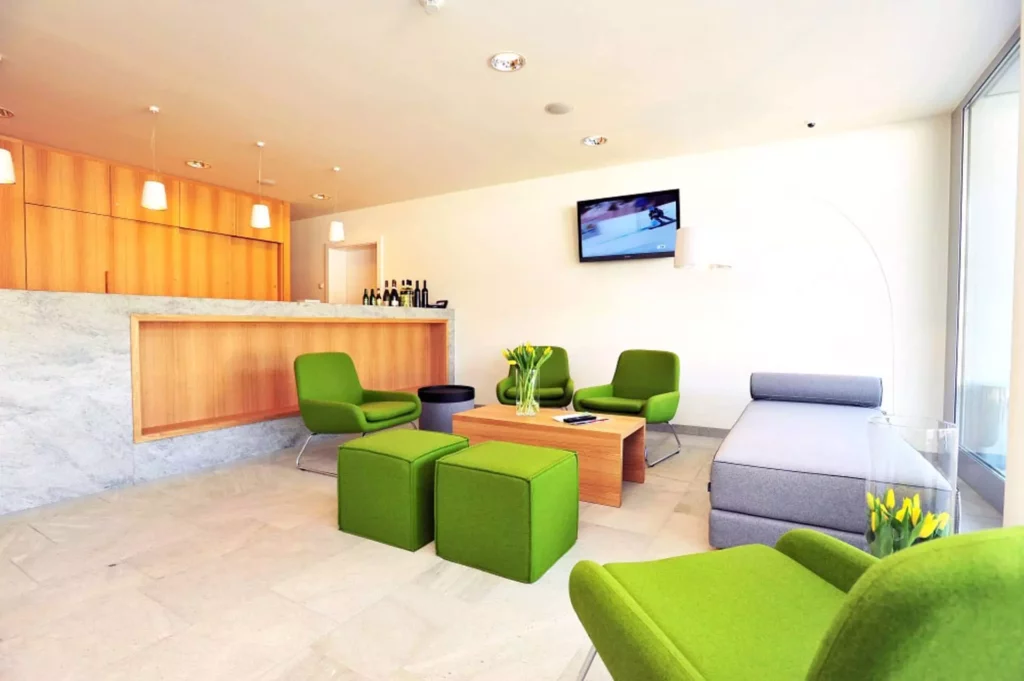 Moderner Wohnraum mit grünen Sesseln und Hockern, grauem Daybed, Holztisch, Bar mit Marmorfront und Wand-TV in, Referenz