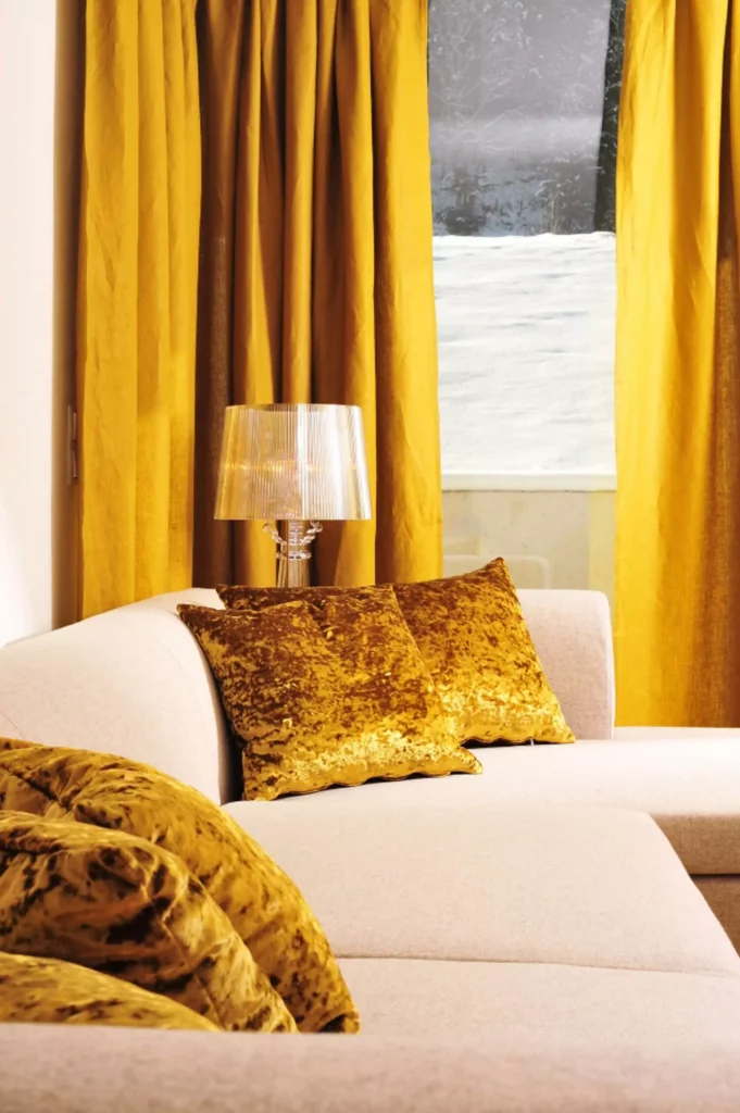 Beige Sofa mit goldgelben Samtkissen vor goldgelben Vorhängen und transparenter Design-Tischleuchte im Innenraum, Referenz