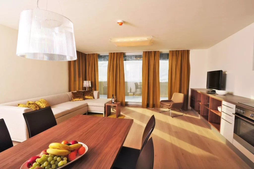 Helles Wohnzimmer mit Ecksofa, goldenen Kissen, Holztisch mit Obstschale, braunen Vorhängen, TV und moderner, Referenz