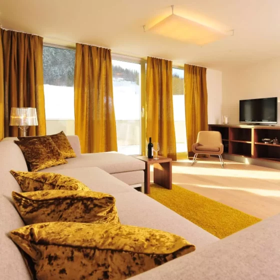 Wohnzimmer mit maßgefertigtem Möbelkonzept, beigem Sofa mit goldgelben Samtkissen, Vorhängen und Teppich, TV-Möbel, Referenz