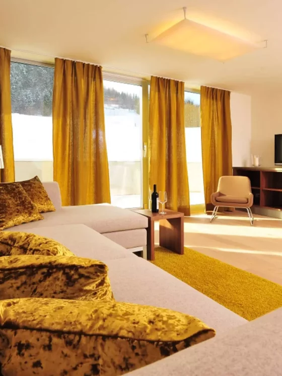 Wohnzimmer mit maßgefertigtem Möbelkonzept, beigem Sofa mit goldgelben Samtkissen, Vorhängen und Teppich, TV-Möbel, Referenz