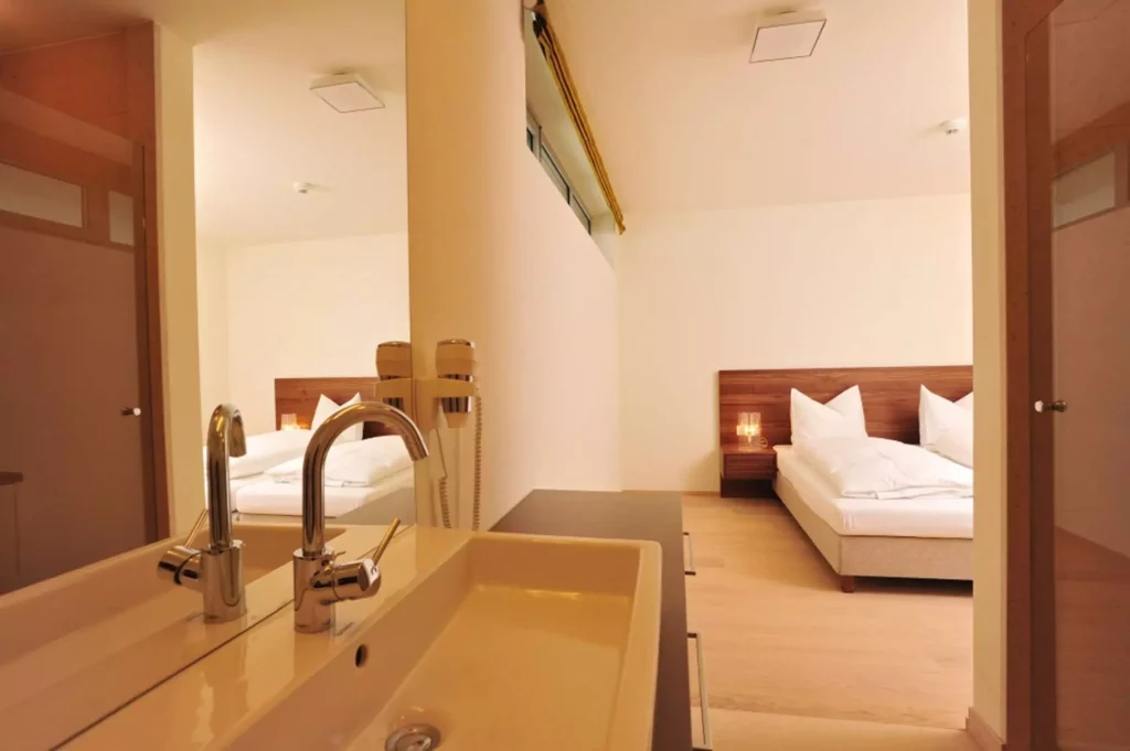 Moderner Wohnraum mit Doppelbett, Holzkopfteil, Nachttisch, integriertem Waschbecken und Spiegelwand in Tauern, Referenz