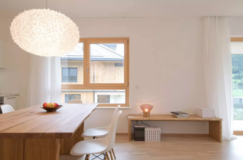 Helles Esszimmer mit massivem Holztisch, weißen Stühlen, großer Designer-Hängelampe und schlichtem Sideboard mit, Referenz