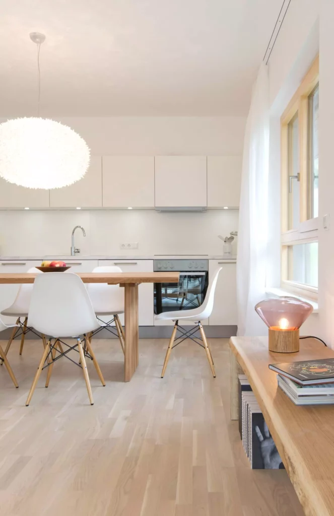 Moderne Ferienwohnung mit weißer Einbauküche, Holztisch, weißen Designstühlen und Holzbank mit Lampe und Büchern in, Referenz