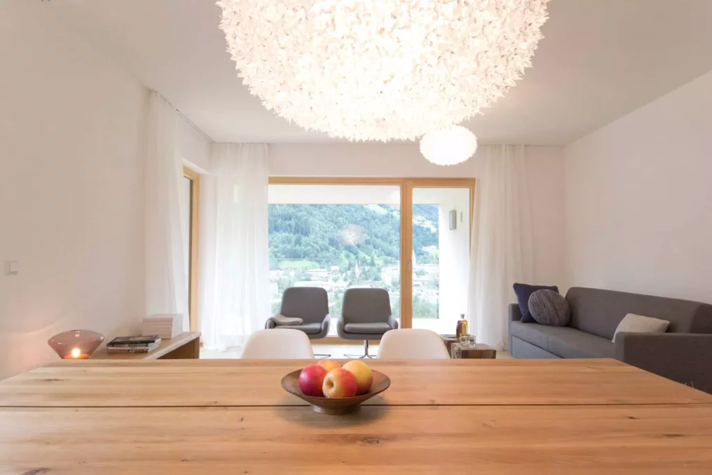 Moderner Wohnraum mit Holztisch, Designermöbeln, großen Fenstern mit Bergblick und dekorativer Deckenleuchte in, Referenz