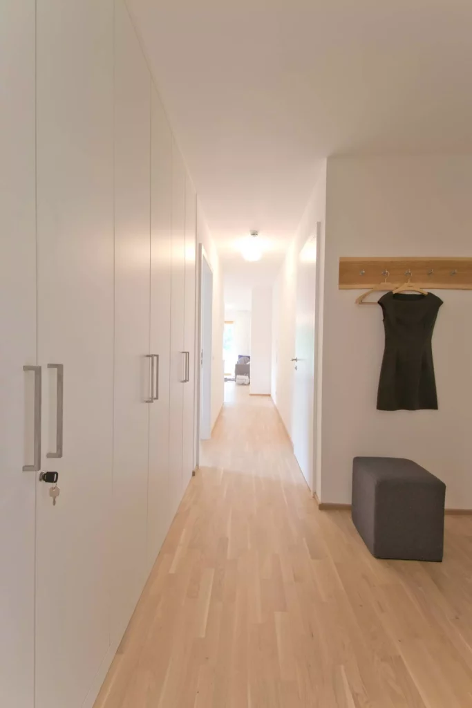 Heller Flur mit maßgefertigten weißen Einbauschränken, Garderobenhaken mit schwarzem Kleid und grauem Sitzwürfel, Referenz
