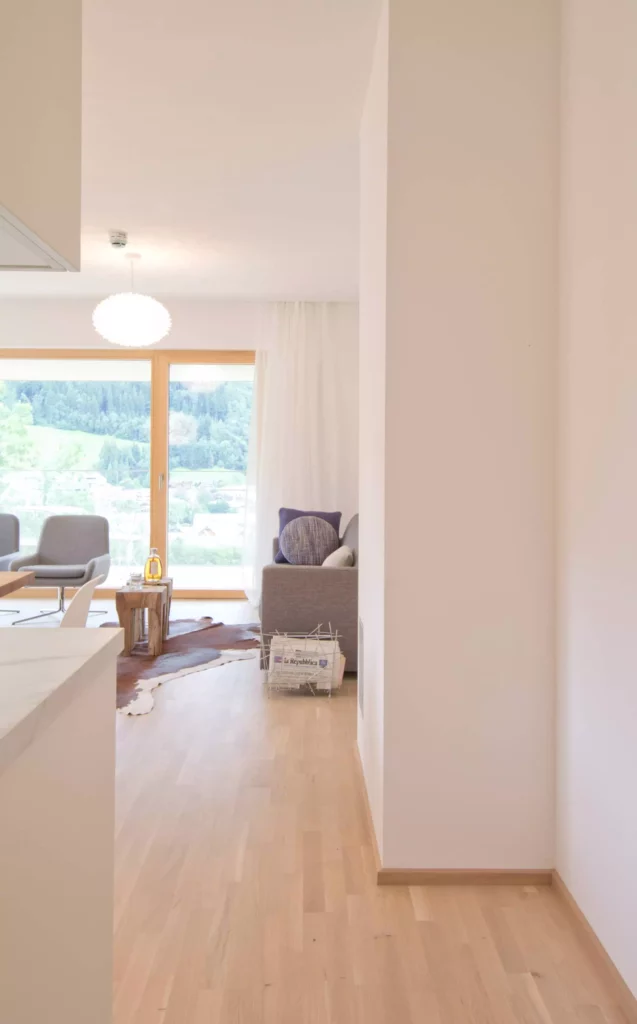 Heller Wohnraum mit Holzfußboden, grauem Sofa mit Kissen, Holzbeistelltisch, Zeitungskorb und großem Fenster mit, Referenz