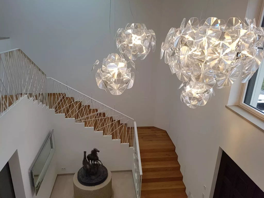 Moderner Treppenaufgang mit Holzstufen, weißem Geländer, drei großen transparenten Designerlampen und Skulptur auf, Referenz