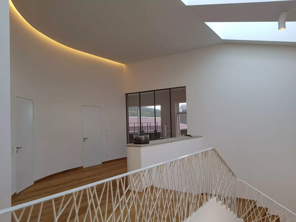 Moderner Innenraum einer Villa in Stuttgart mit weißer Wandverkleidung, Holztreppe, indirekter Deckenbeleuchtung, Referenz