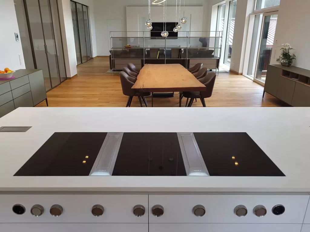 Moderne offene Küche mit Bora Kochfeld auf weißer Insel, Holztisch mit Lederstühlen und Designermöbeln in Villa, Referenz