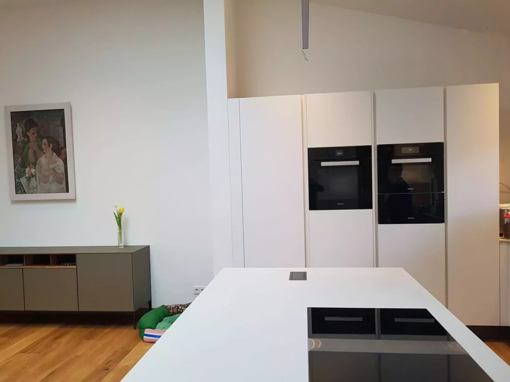 Moderne weiße Küche mit Einbaugeräten von Miele, weißer Kochinsel, Sideboard, Holzfußboden und Kunst an der Wand, Referenz