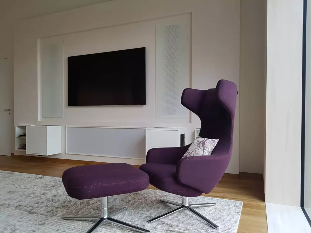 Moderner lila Design-Sessel mit Hocker vor maßgefertigter weißer Wandverkleidung und TV in einer Villa in Stuttgart, Referenz