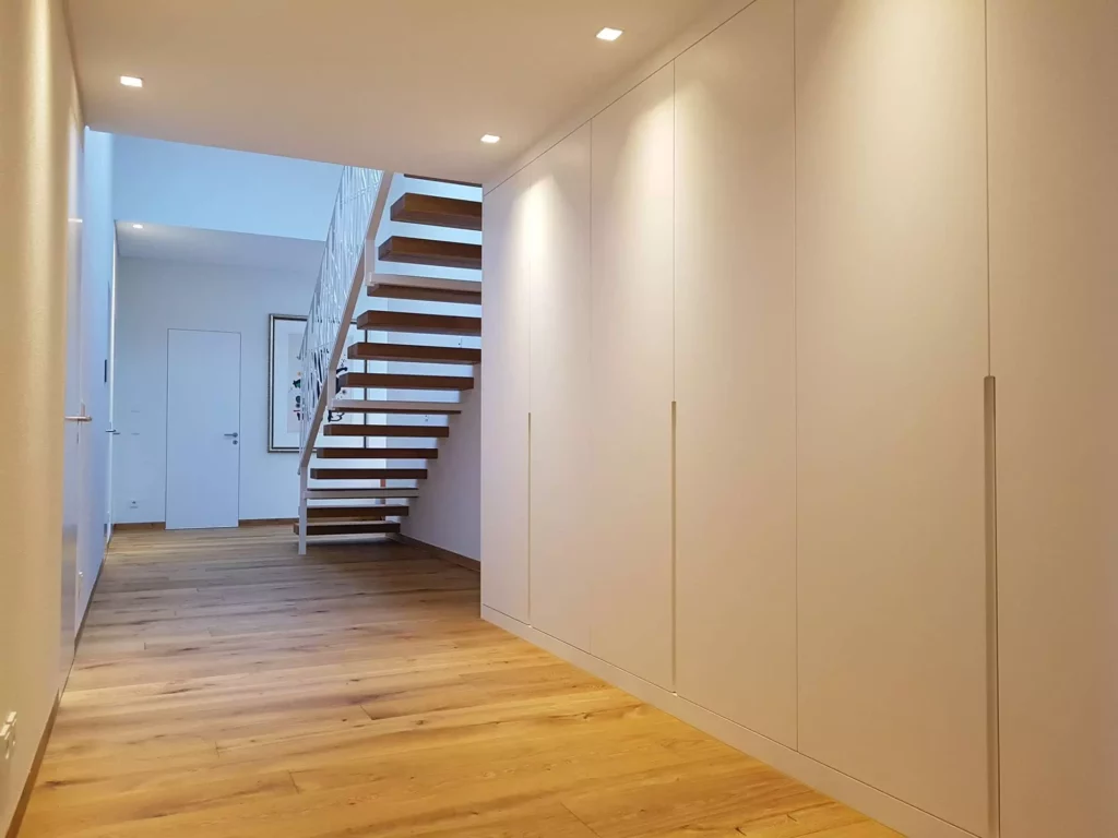 Moderner Flur mit maßgefertigter weißer Wandverkleidung und freitragender Holztreppe in einer Villa in Stuttgart, Referenz