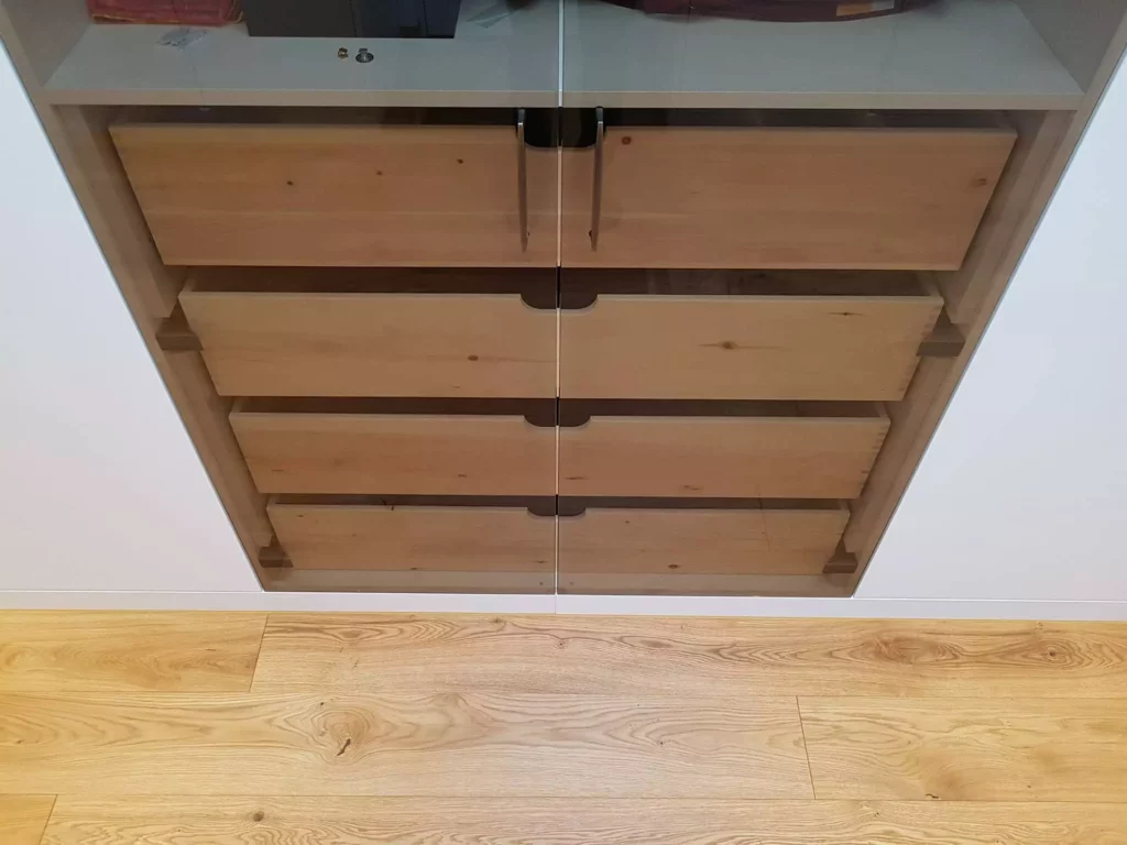 Maßgefertigte Holzschubladen mit Griffmulden hinter Glasfront in moderner Innenarchitektur mit Parkettboden, Referenz