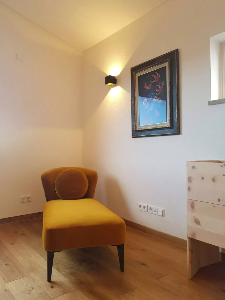 Gelber Polstersessel mit rundem Kissen vor weißer Wand mit Wandlampe und gerahmtem Bild in modernem Wohnraum mit, Referenz