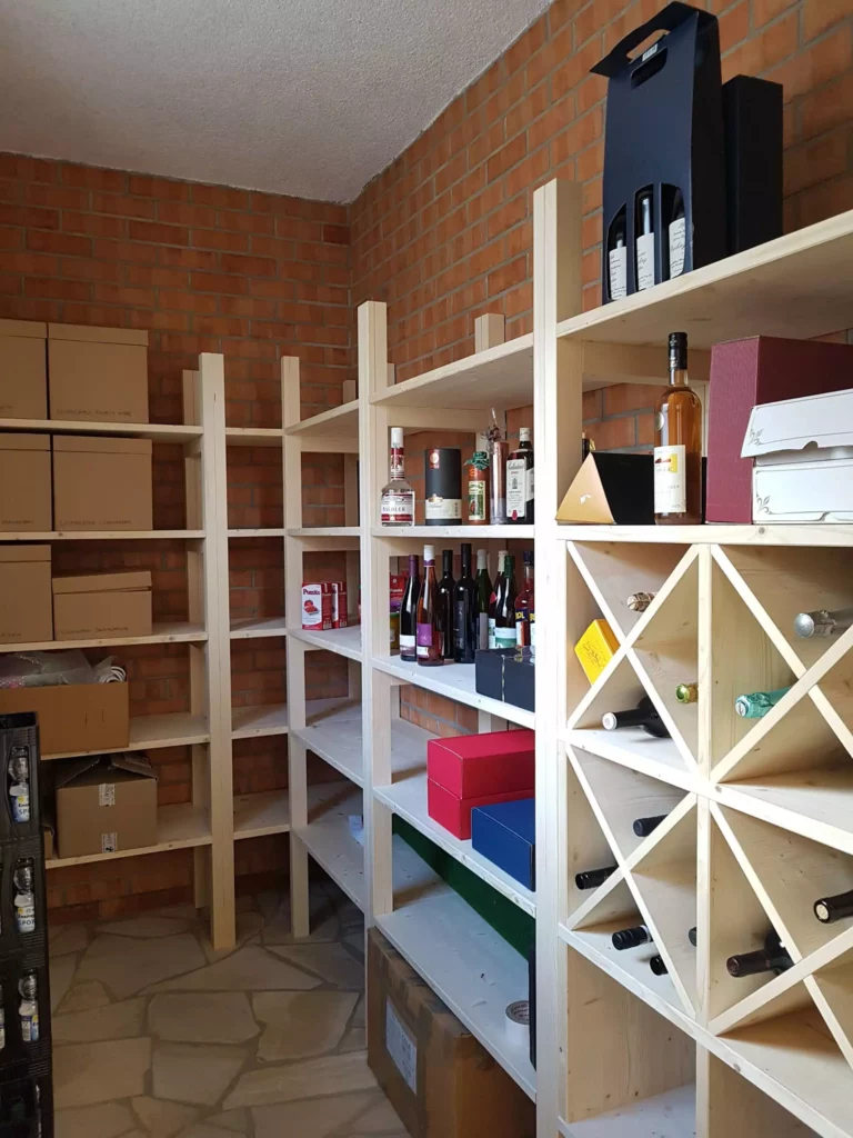 Holzregale mit Weinflaschen, Spirituosen und Kartons vor roter Ziegelwand in einem Kellerraum, maßgefertigte, Referenz
