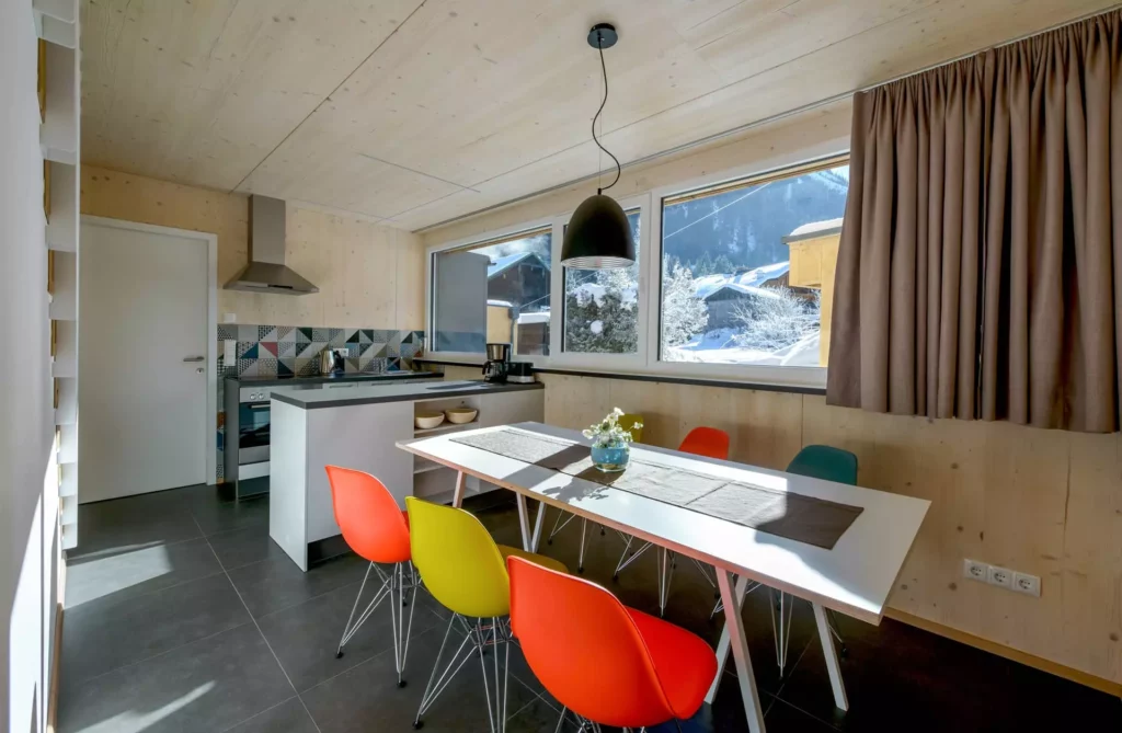 Moderne Küche mit Vitra DSR Stühlen in bunten Farben, weißem Tisch, Holzverkleidung und großem Fenster mit, Referenz