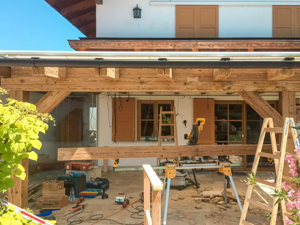 Baustelle mit Altholzverbau und Tischlerwerkzeugen vor Haus mit Fensterläden, Leiter und Arbeitsgeräten im, Altholzmöbel