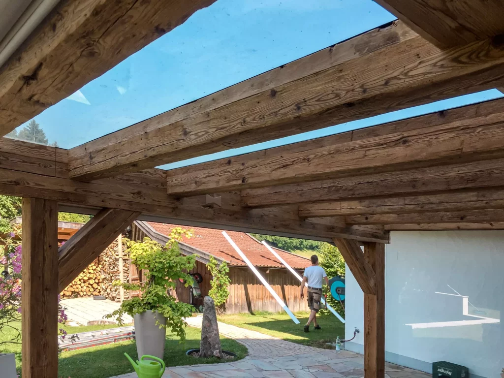 Altholzverbau mit Glasdach und sichtbaren Holzbalken in Außenbereich einer Tischlerei mit Mann im Hintergrund, Altholzmöbel